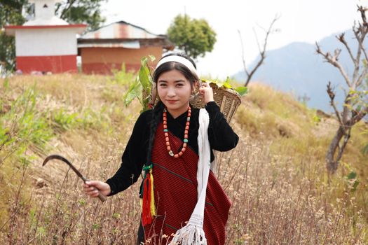 Portrait of a Nepalese woman in traditional attire carrying a basket in a rural landscape.