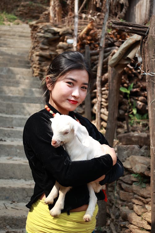 Brunette in a Village, Holding a Baby Goat