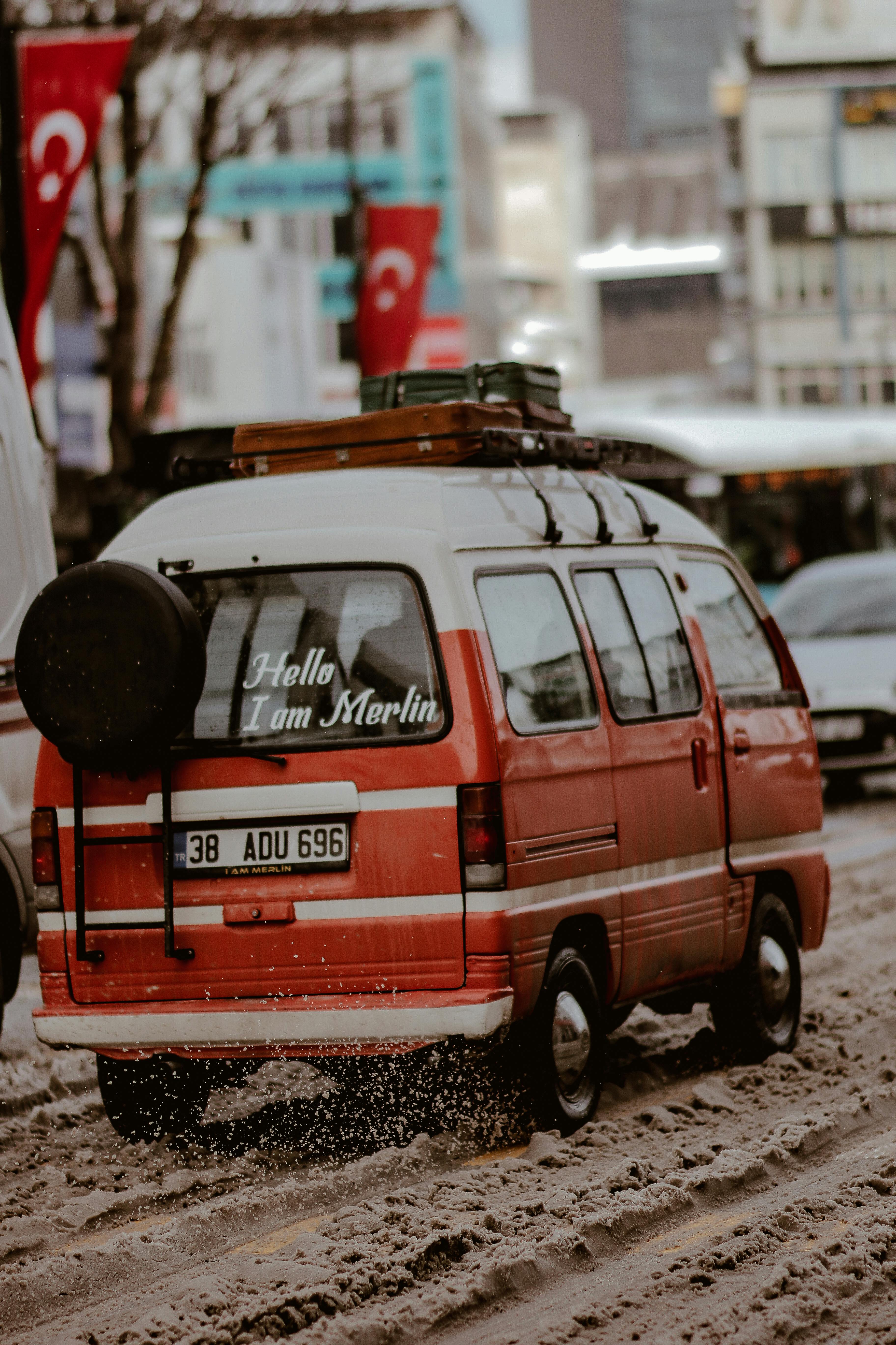 A nostalgic red van labeled 'Hello, I am Merlin' moves through snowy city streets, showcasing a retro winter vibe.