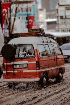 A nostalgic red van labeled 'Hello, I am Merlin' moves through snowy city streets, showcasing a retro winter vibe.