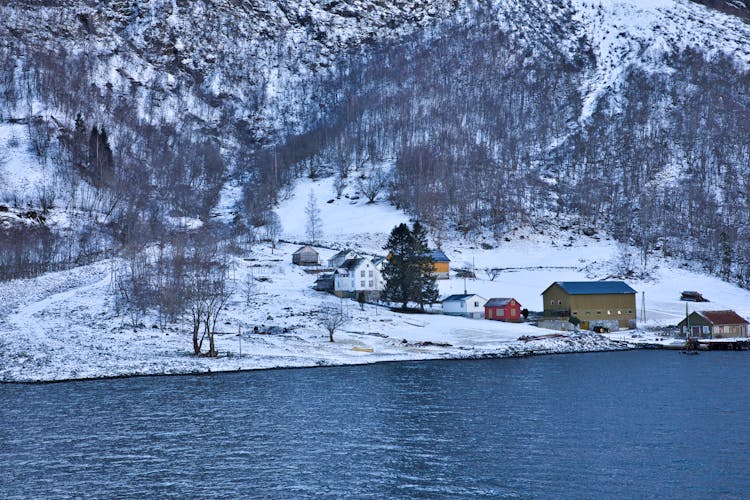 House On River Bank In Winter Mountains Landscape