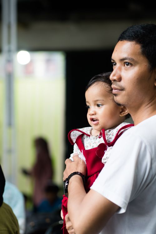 Free A touching portrait of a father holding his baby daughter at an indoor event. Stock Photo