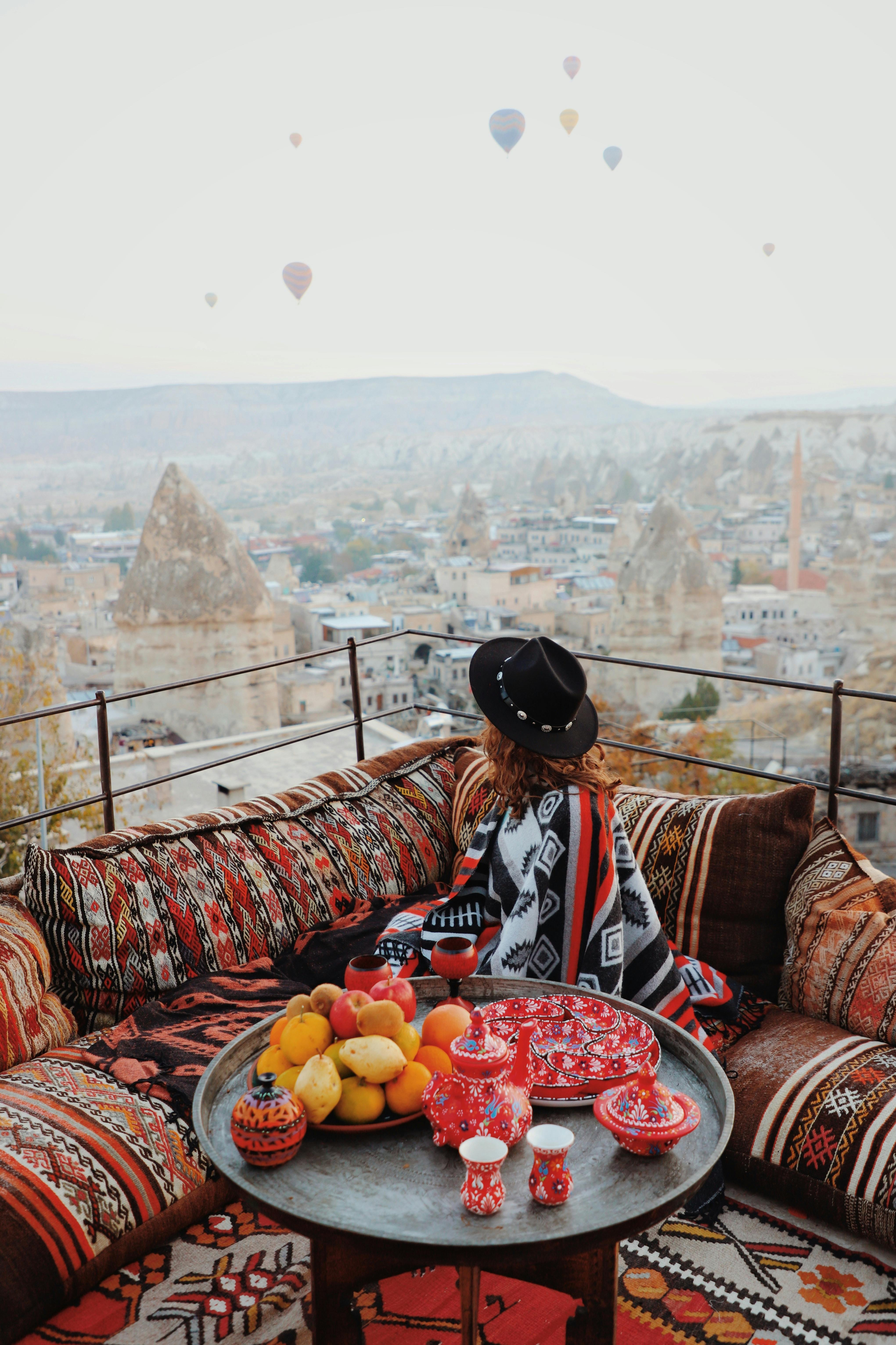 Woman enjoys Cappadocia's landscape from a vibrant terrace overlooking hot air balloons and unique formations.