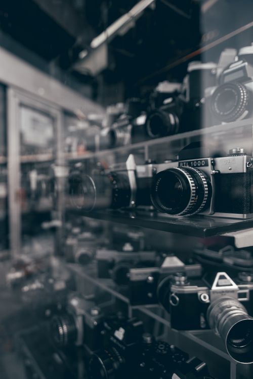 Free A collection of vintage cameras displayed behind glass with reflective surfaces. Stock Photo