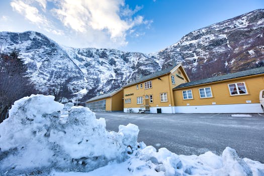 Yellow houses in a snowy valley with mountains, icy road, and blue sky.