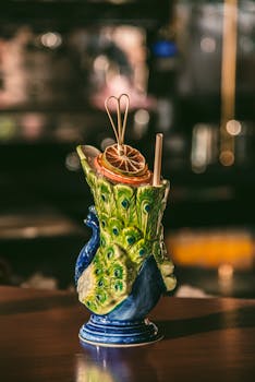 Vibrant cocktail in peacock-shaped mug with dried citrus slice garnish.