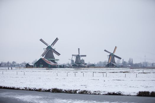 A picturesque winter scene of windmills at Zaanse Schans, Netherlands, covered in snow.
