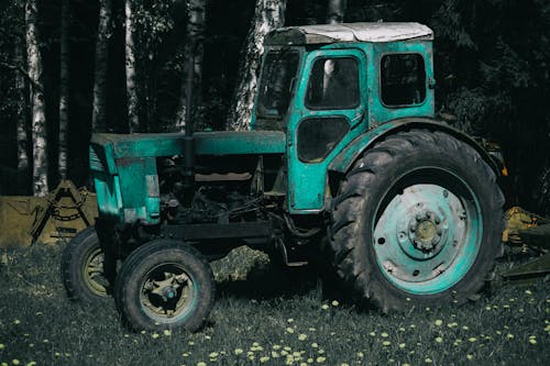 Photo of an Abandoned Turquoise Tractor by a Forest