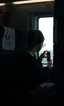 A young woman uses her smartphone to capture views from a train window, framed in a candid moment of travel.