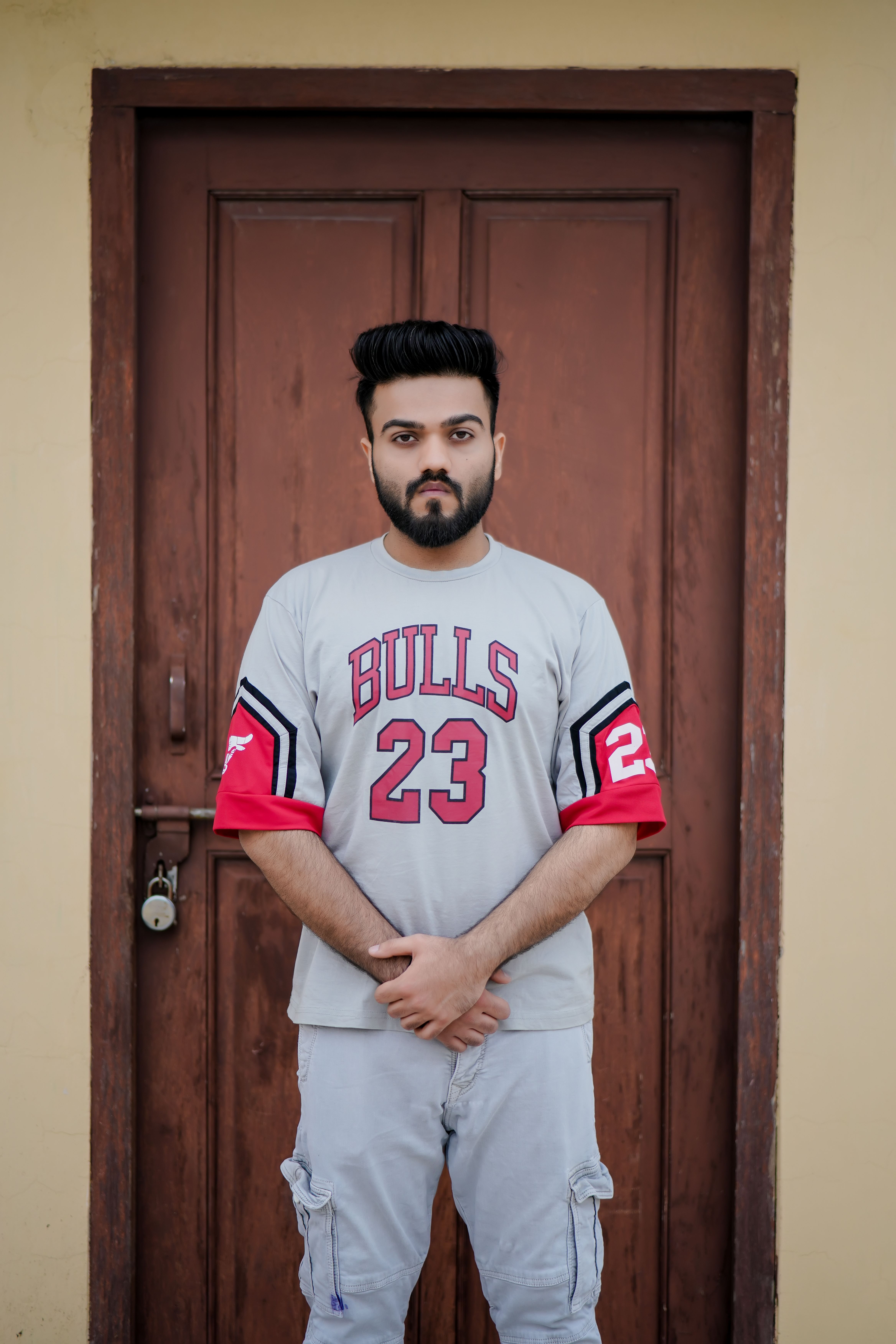 Young man in a sports t-shirt poses confidently in front of a wooden door, showcasing casual style and attitude.