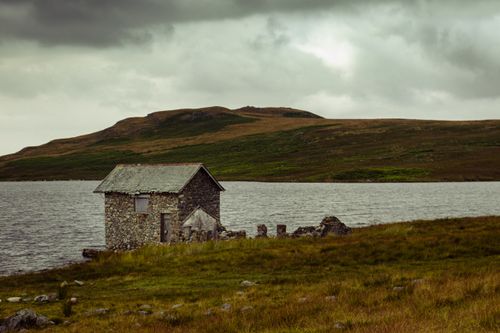 Free A beautiful stone house sits by a peaceful lake under an overcast sky, embodying the serenity of autumn landscapes. Stock Photo