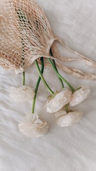 Delicate white peonies elegantly displayed in a mesh bag on soft white linen, evoking a sense of minimalist style.