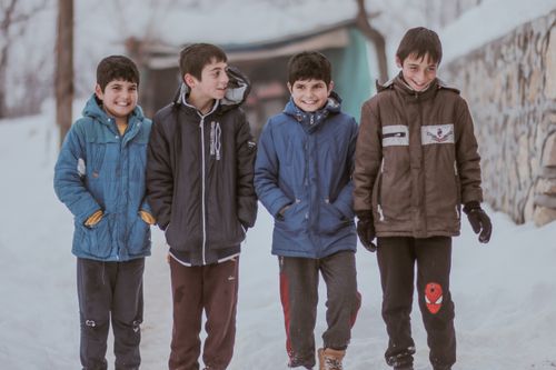 Free Four cheerful boys in winter jackets walking and smiling in a snowy outdoor setting. Stock Photo