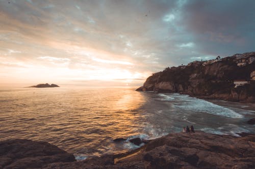 People Sitting Near Cliff Beside Body of Water Photograph