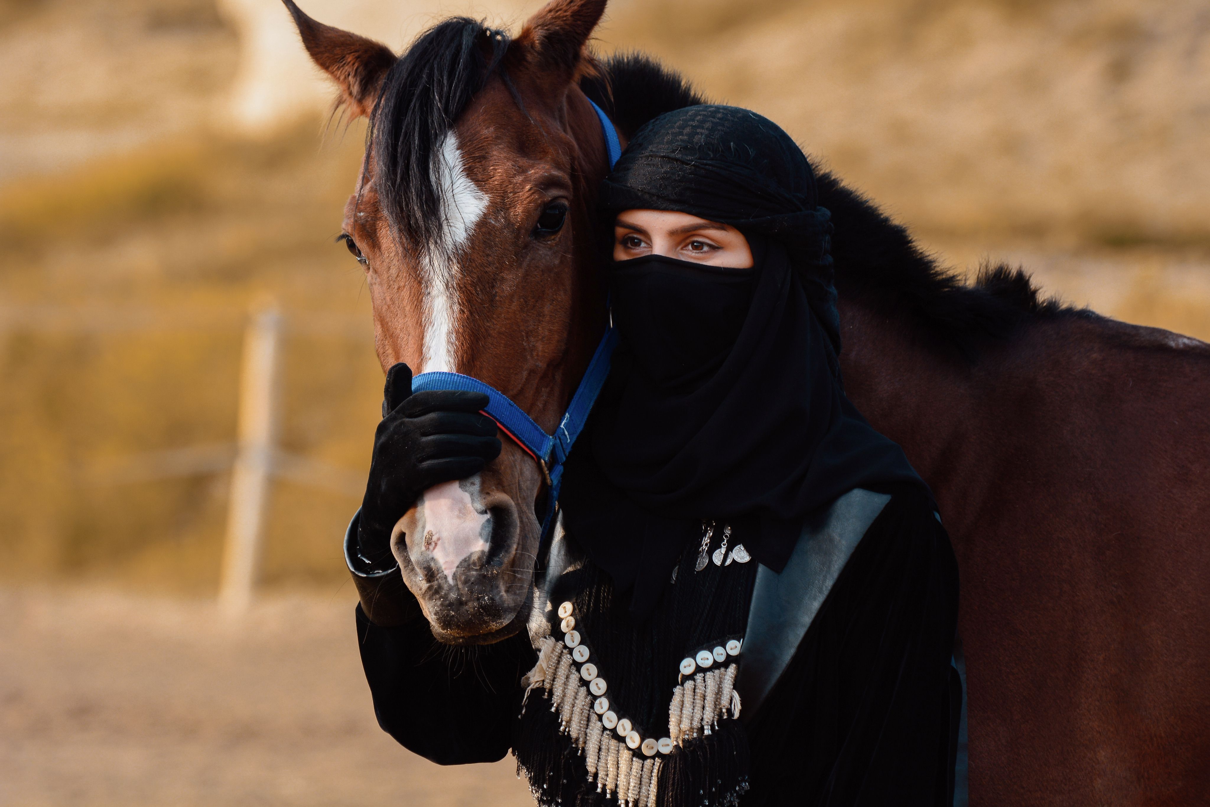 A woman in traditional clothing poses with a horse in a desert landscape.