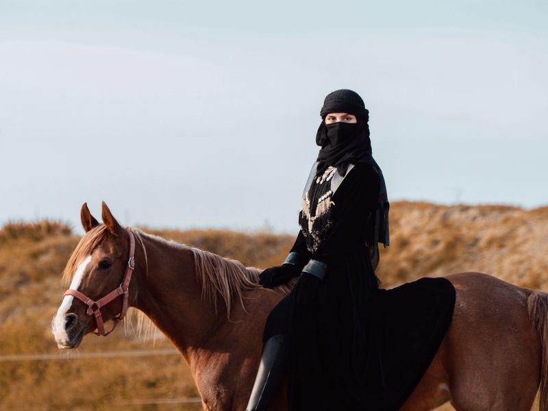 Woman in traditional dress riding a chestnut horse in the desert