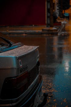 Glistening city street captured at night featuring a car parked in the rain.