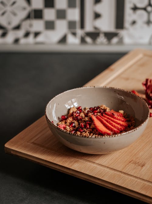 Gray Bowl of Cereals and Sliced Red Strawberries, on a Wooden Cutting Board