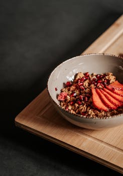 A delicious breakfast bowl with strawberries and granola on a wooden board.