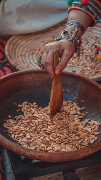 A traditional roasting process using a wooden spoon to stir seeds in a rustic bowl.