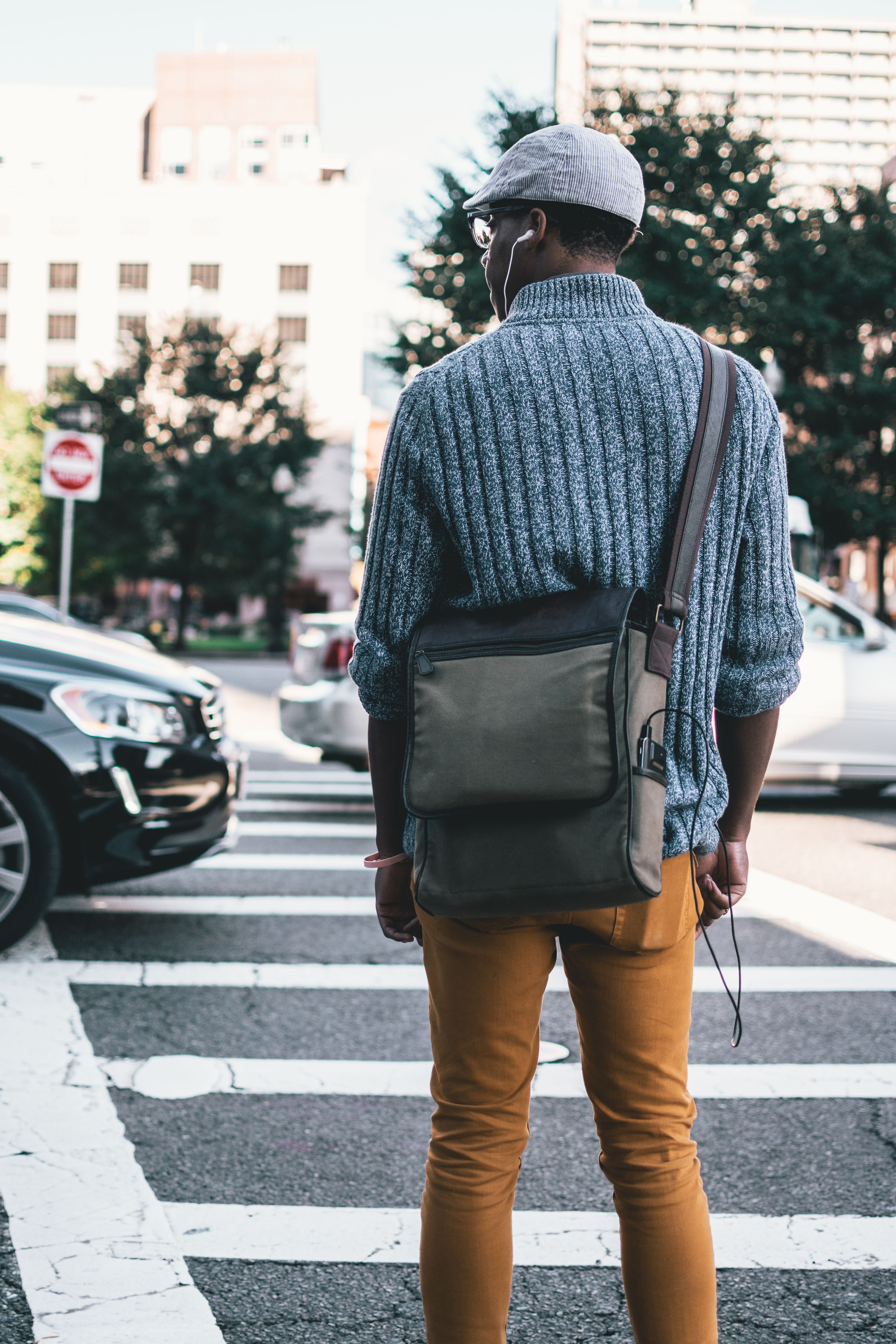 Back view of a man wearing casual clothing crossing an urban street at a crosswalk.