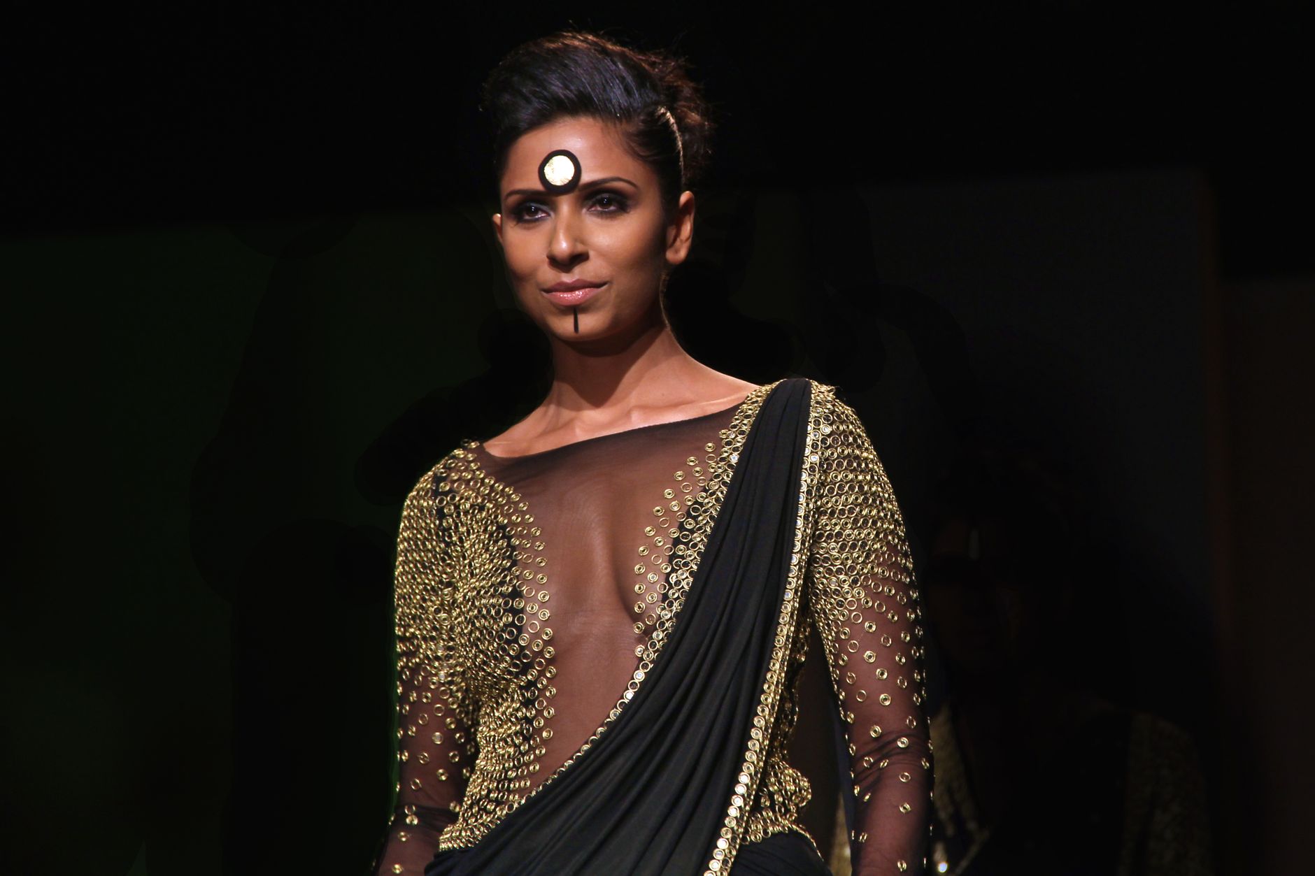 Portrait of a fashion model with artistic makeup and intricate attire on a black background.