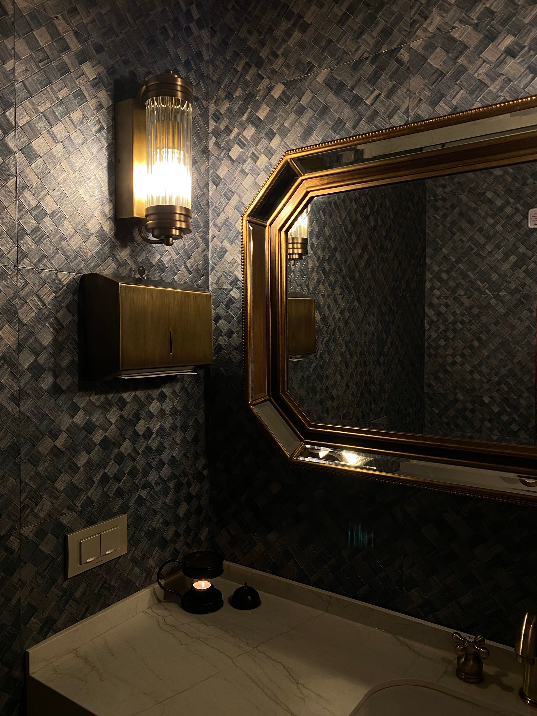 Bathroom with geometric wall tile, framed mirror and warm decorative lighting