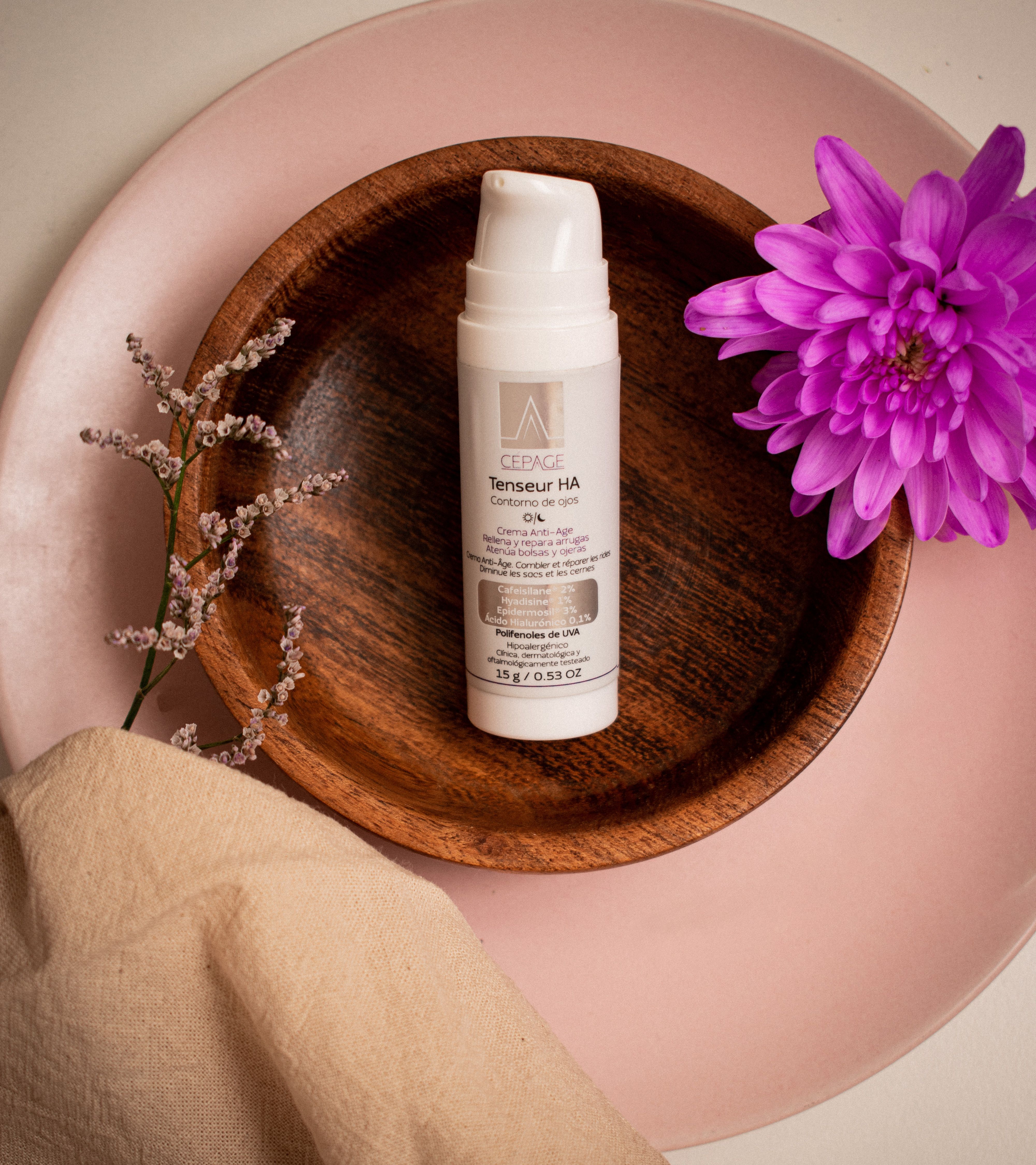 Cosmetic cream bottle on a wooden bowl with flowers and fabric decor.