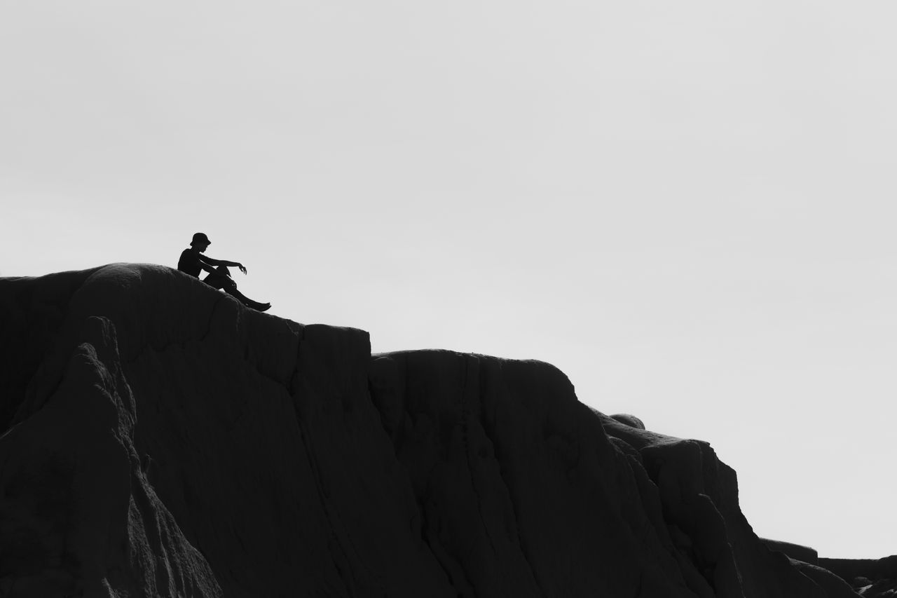 silhouette of a man sitting atop cliffs at canoa quebrada brazil evoki