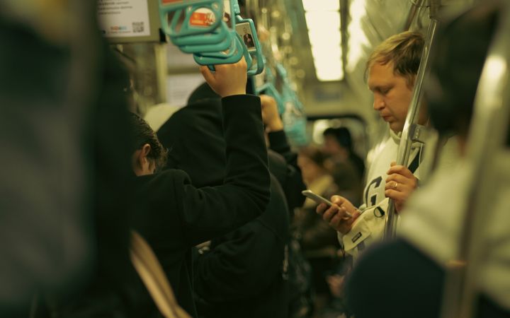 A crowded subway train with commuters standing and using phones, showcasing urban life.