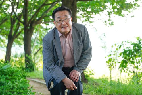 Free An elderly man wearing a jacket leans forward in a green park setting during summer. Stock Photo