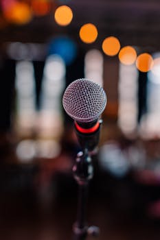 A microphone in focus with blurred bokeh lights in the background, creating a vibrant nightlife atmosphere.