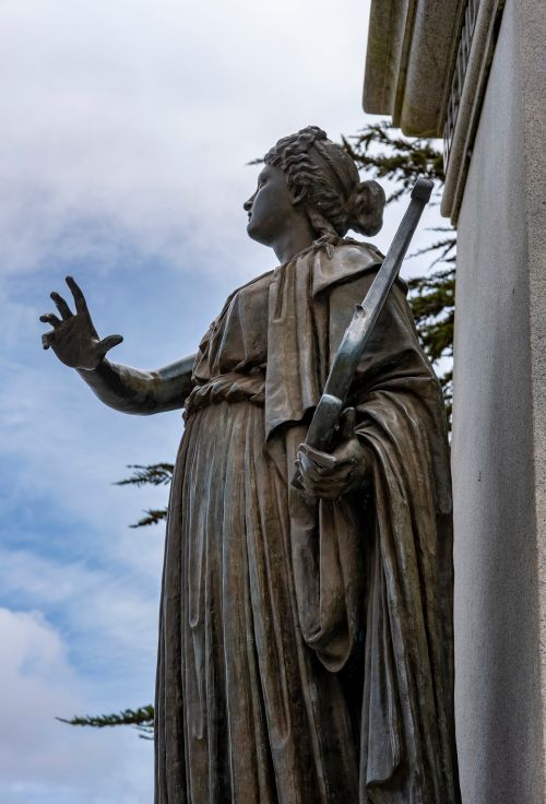 Free A majestic marble sculpture of a woman in robes against a cloudy sky. Stock Photo