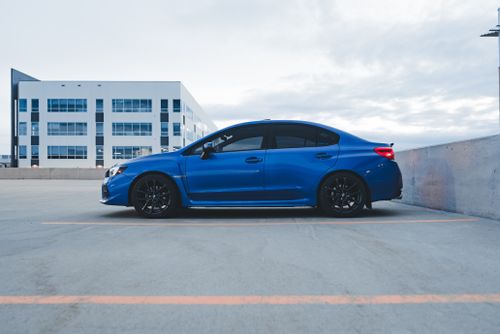 Free A stylish blue sports car parked in an empty urban parking lot under cloudy skies. Stock Photo