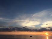 宁静的日落图像中，平静的海面上，划艇与云彩共同营造出一片宁静的海景