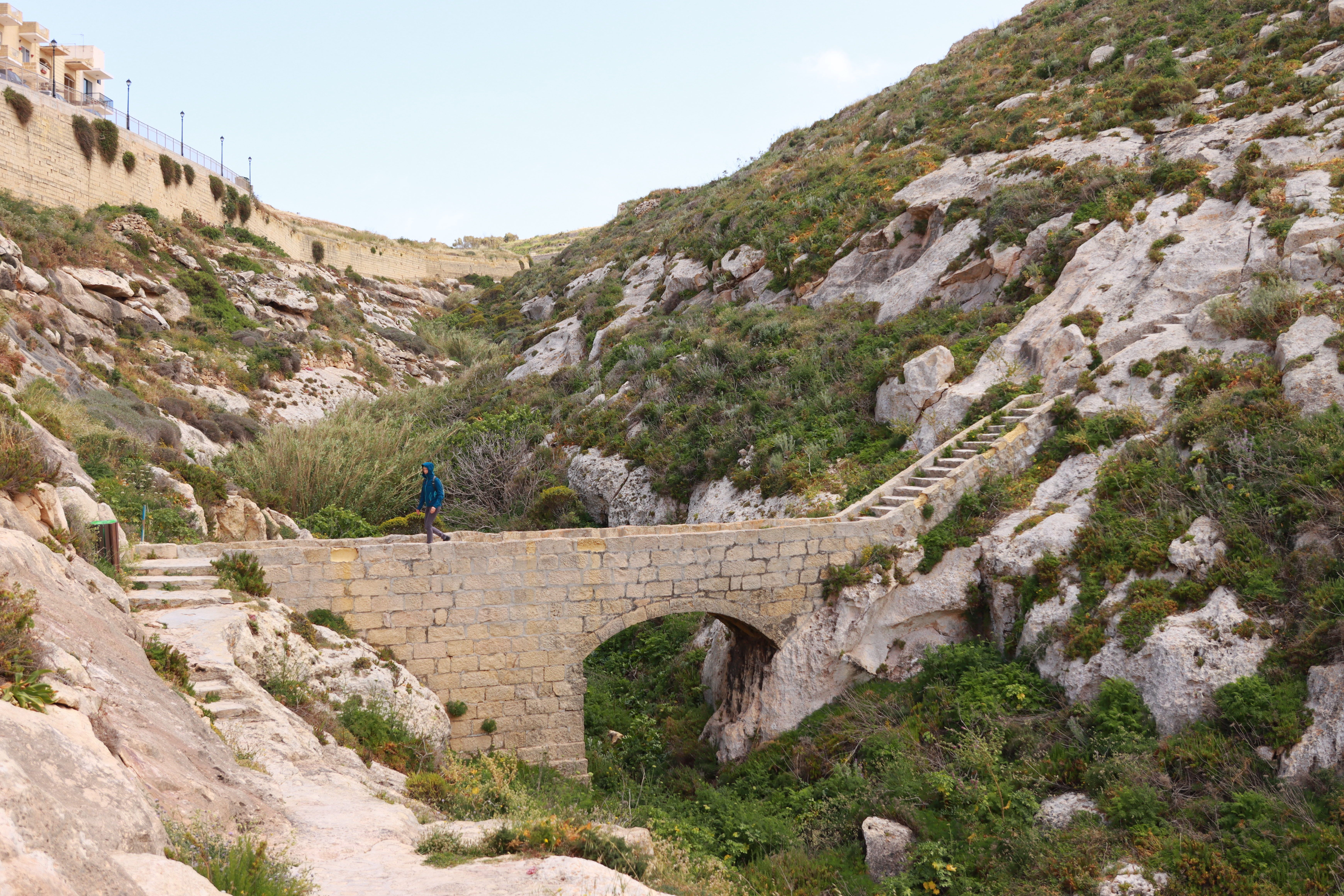 Scenic view of a historic stone bridge amidst Malta's rugged countryside.