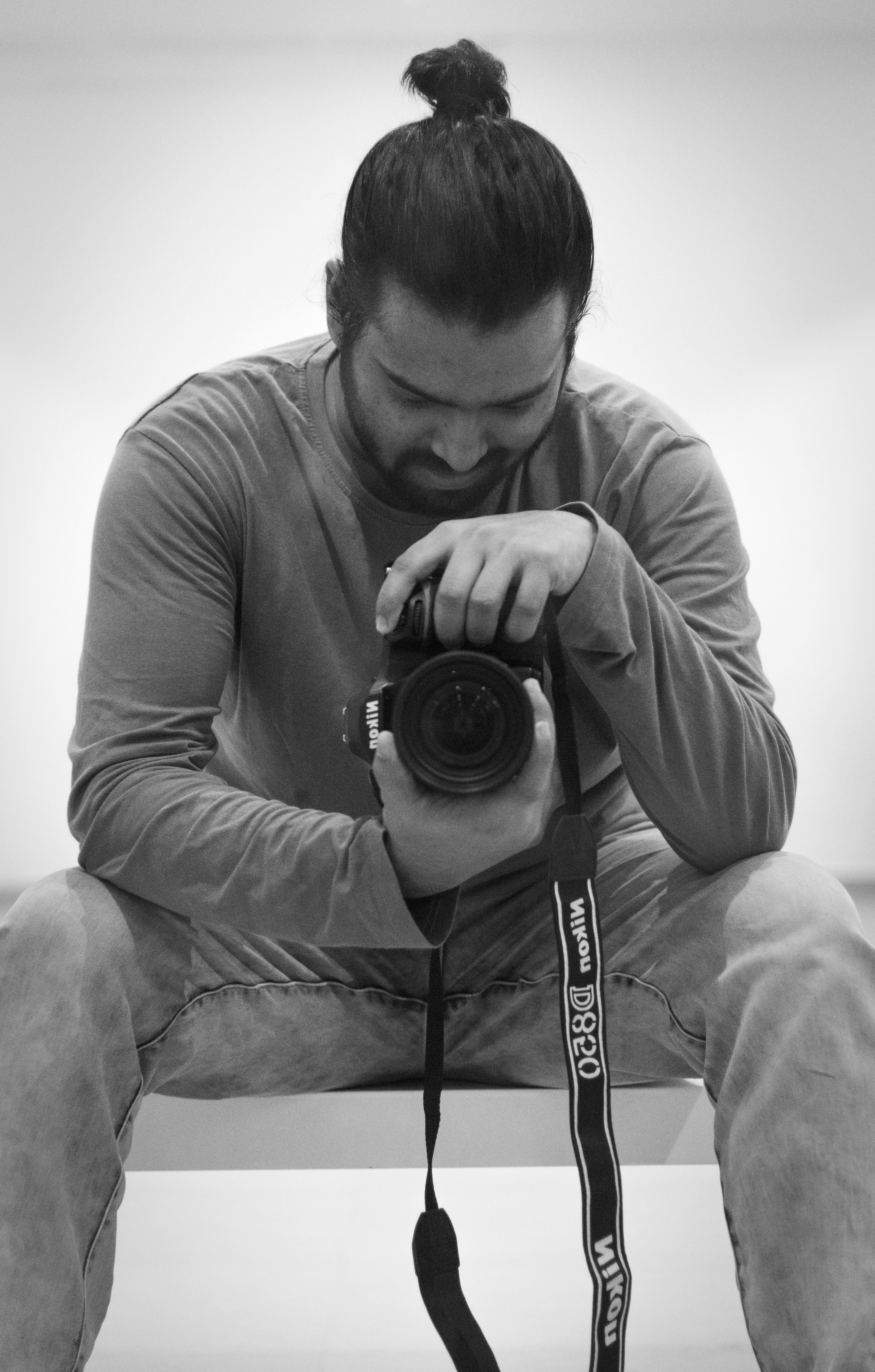Black and white portrait of a seated photographer holding a camera, in a thoughtful pose.