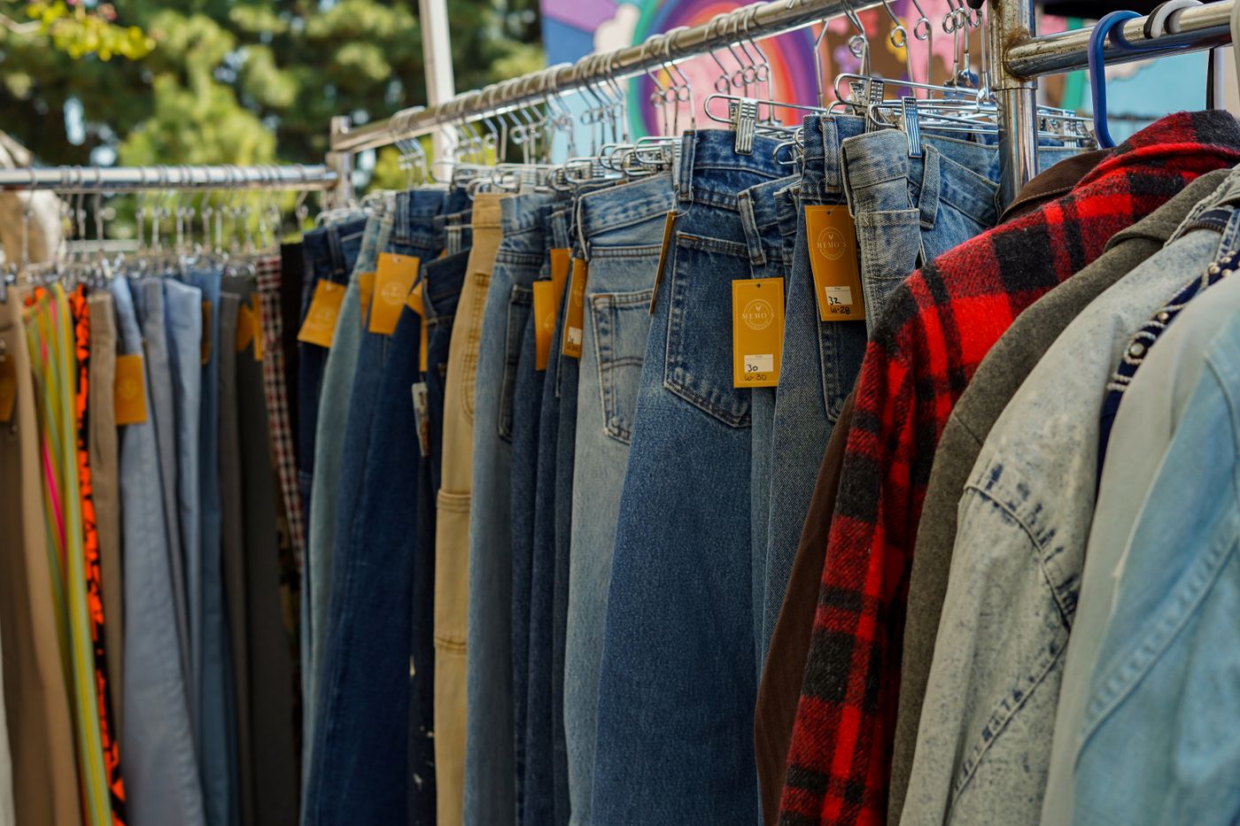 Rack of vintage jeans and shirts with price tags at an outdoor flea market