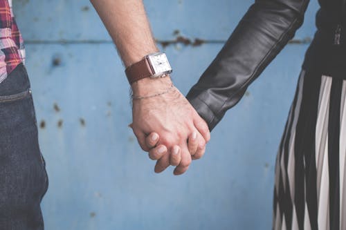 2 Person Holding Hands Besides Blue Painted Wall