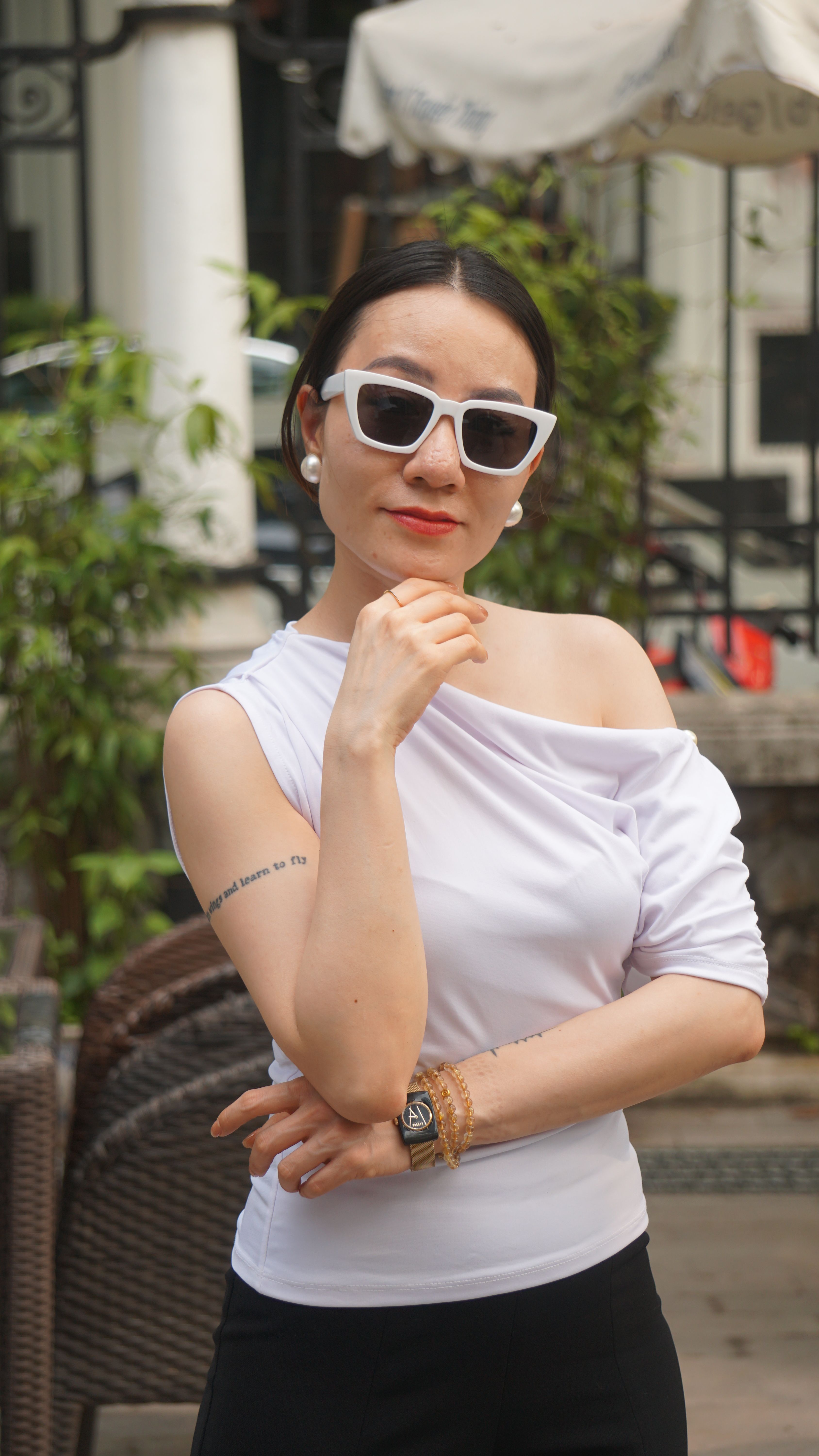Fashionable woman in white outfit and sunglasses posing confidently outdoors.