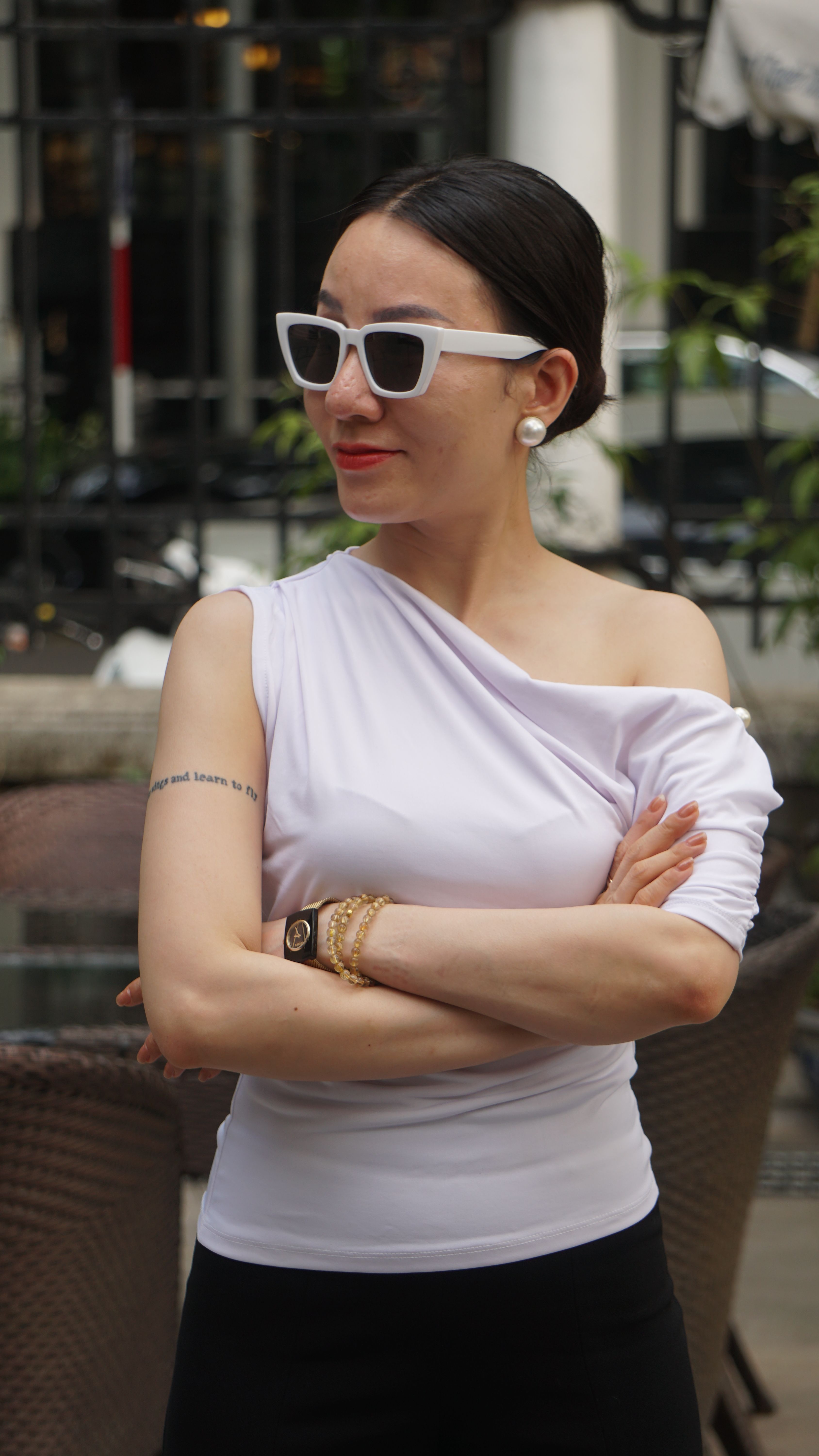 Elegant woman in a white top and sunglasses posing confidently outdoors, showcasing her fashion sense.