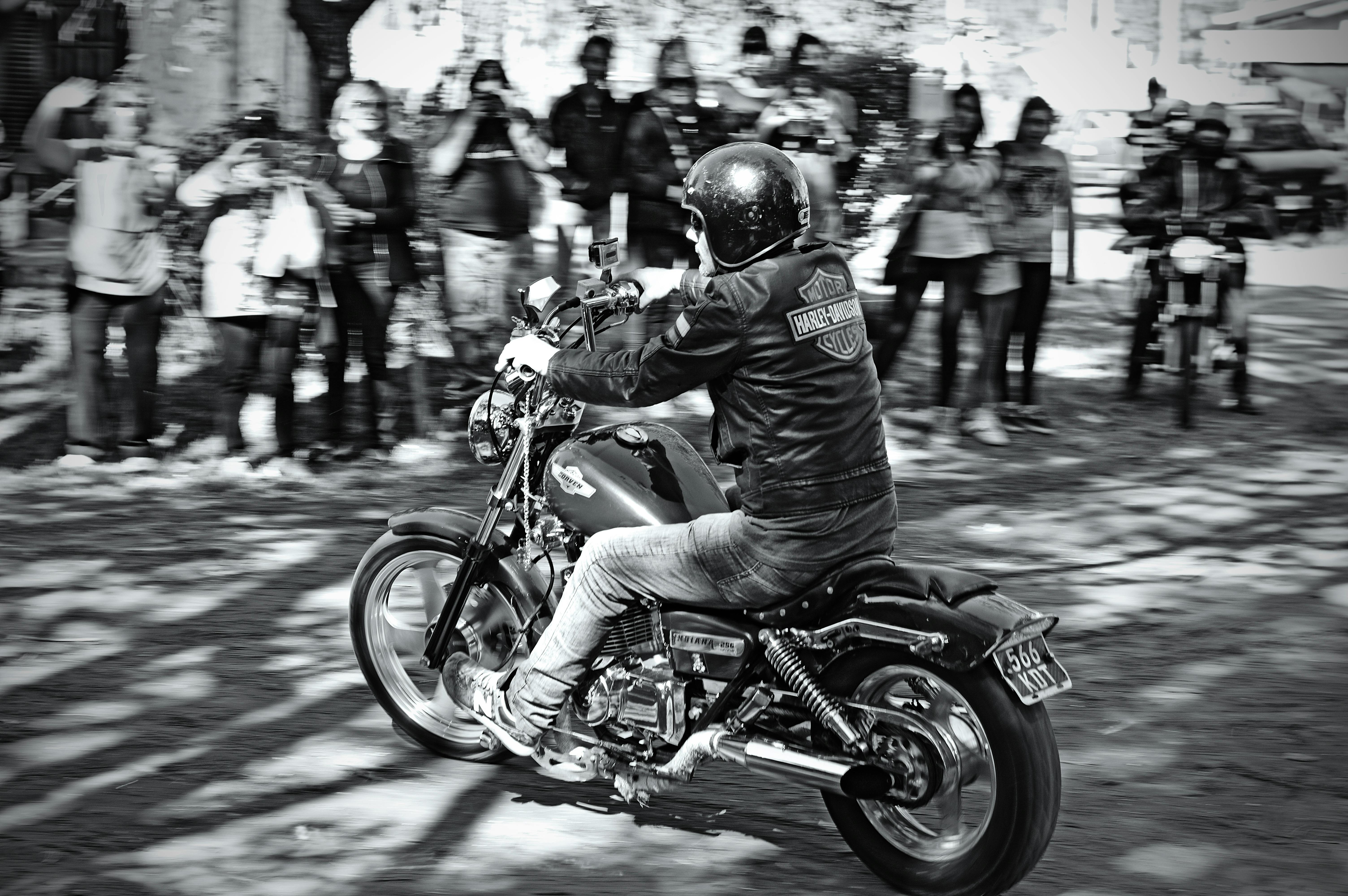 Black and white photo of a biker in a helmet on a motorbike amid city event crowds.