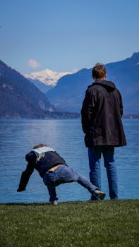 Two men by a serene lake with snow-capped mountains and blue skies.