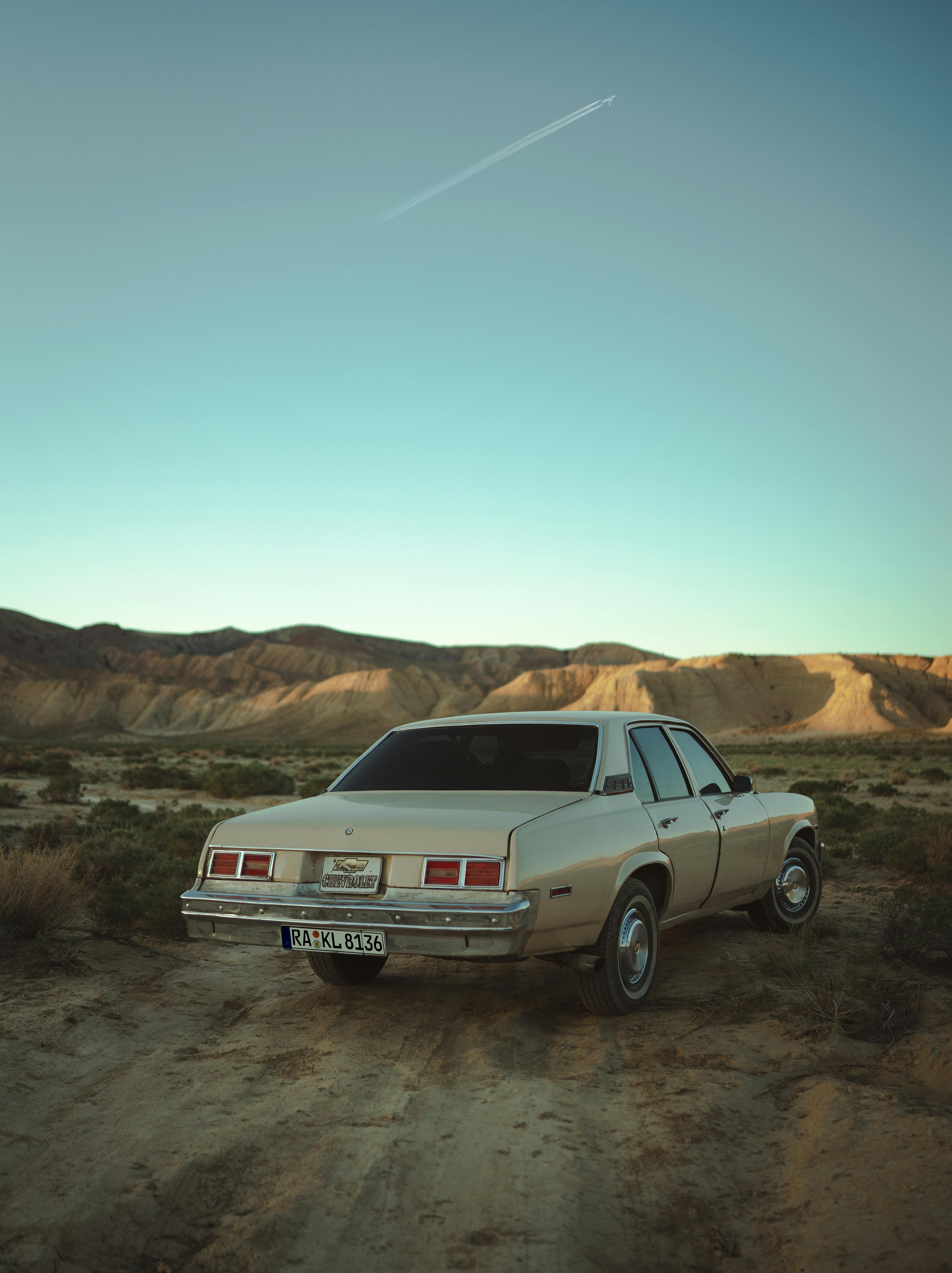 A classic vintage car parked on a desert dirt road during sunset with clear skies.