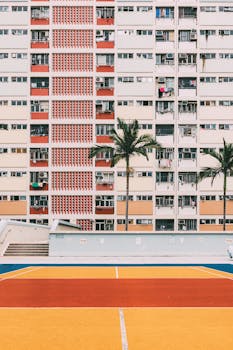 A vibrant urban basketball court against high-rise residential buildings with palm trees.
