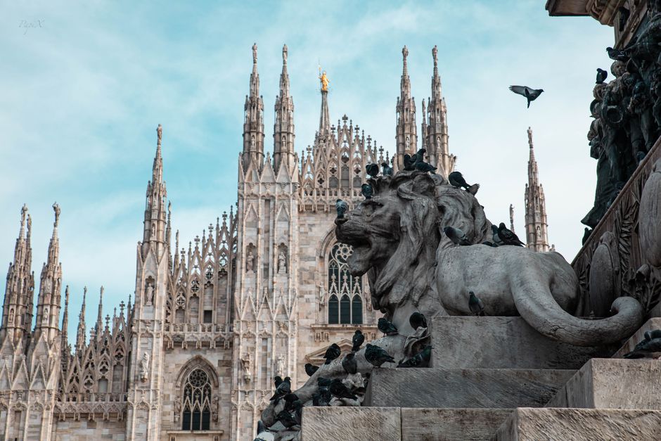 View of the iconic Milan Cathedral with a lion statue in the foreground. Classic gothic architecture.