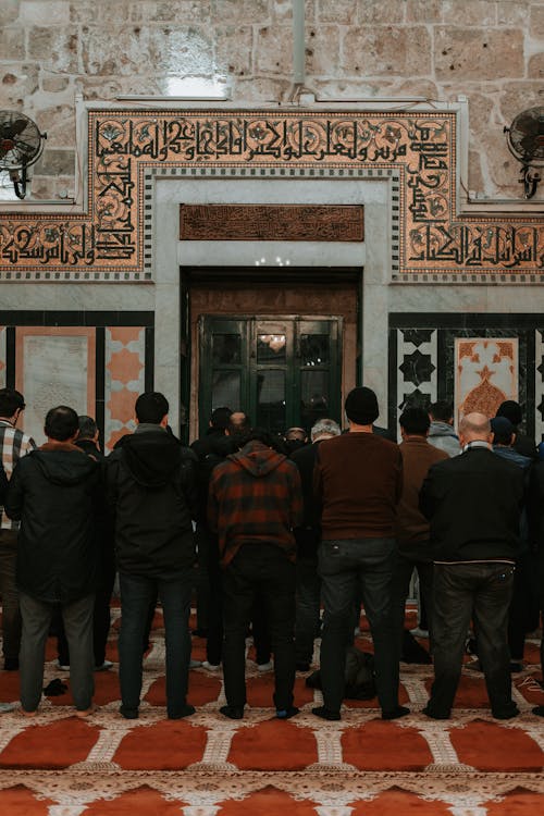 People standing in a mosque with arabic writing on the wall