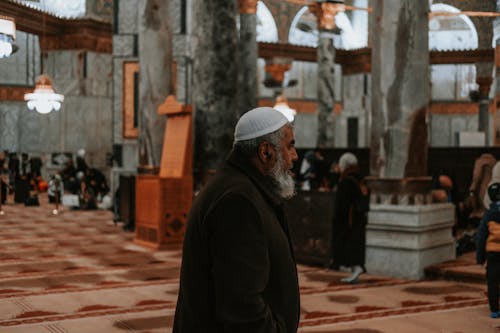 A man in a white hat is walking through a mosque