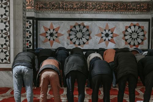 Free A group of people praying inside a beautifully decorated mosque with intricate Islamic art. Stock Photo