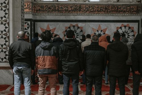 Free A group of men praying inside a beautifully decorated mosque with intricate artworks on the walls. Stock Photo